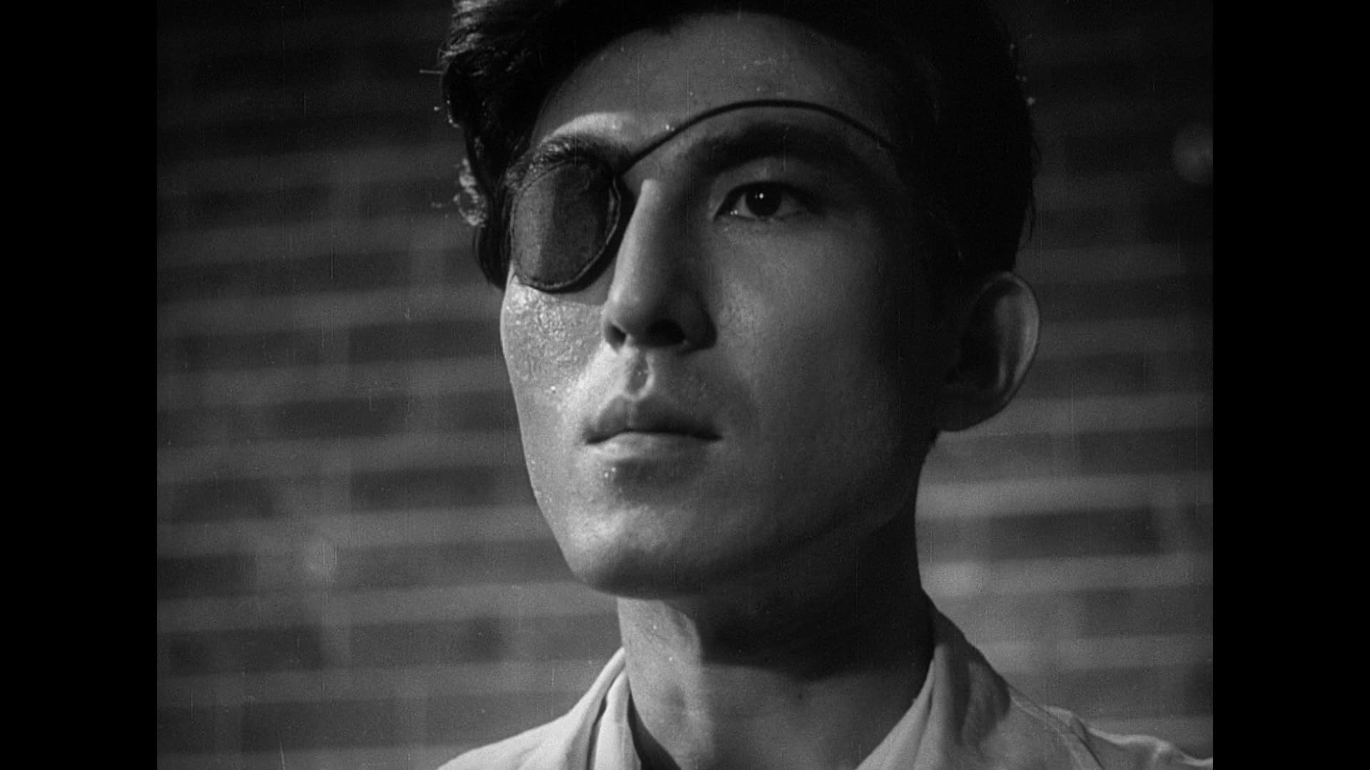 A stern man looking to the left of the camera, his right eye covered with an eyepatch
