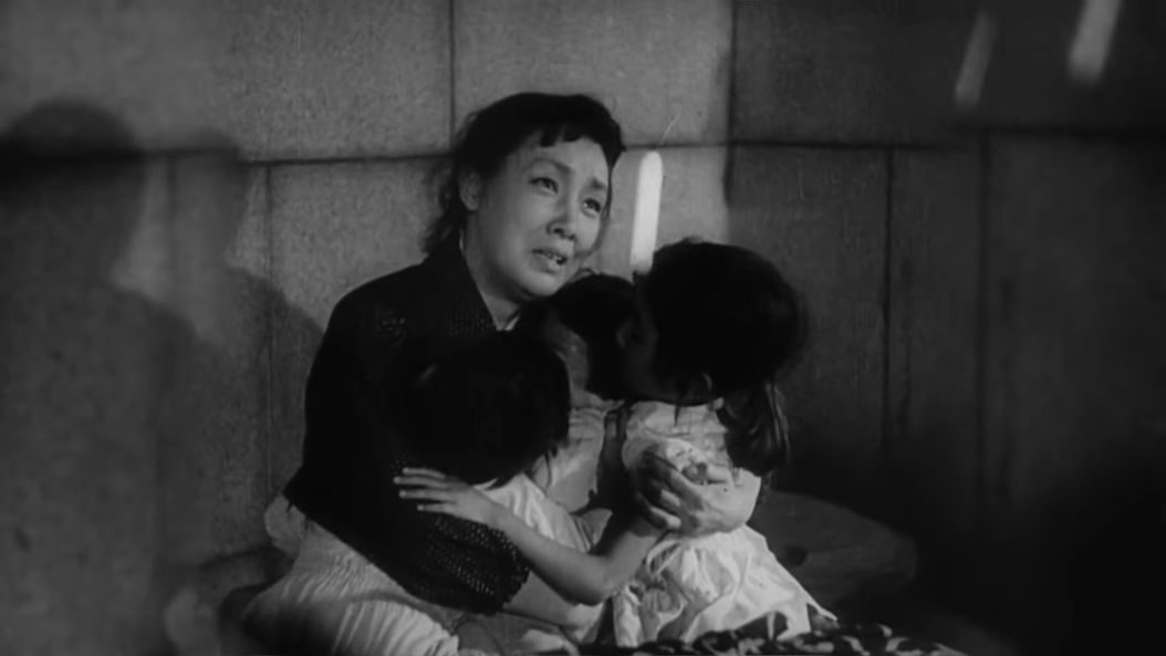 A woman holding her children close to her, a look of fear on her face